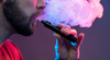 A man exhaling vapour while holding a vape pen